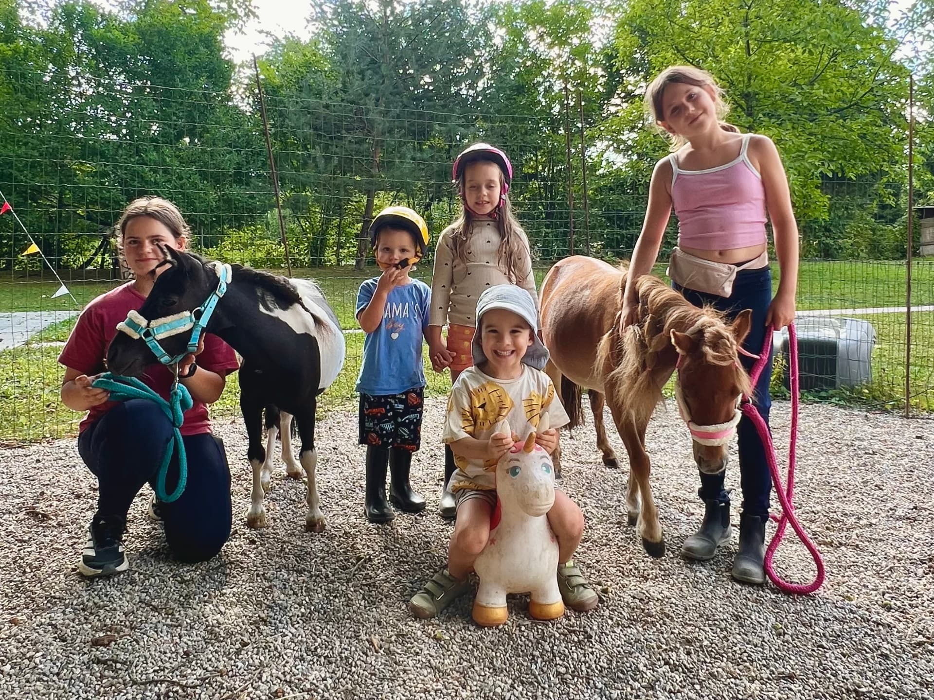 Skupina otrok pozira z dvema mini ponijema in igračo samorogom
